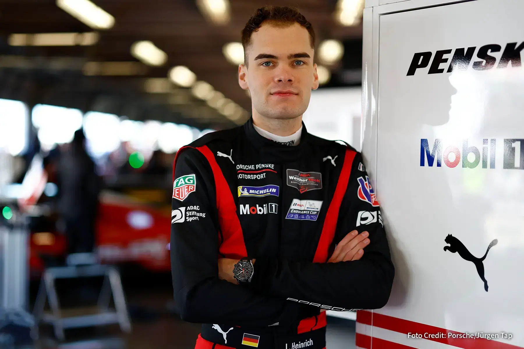 Porsche Rennfahrer Laurin Heinrich im Motorsport Anzug steht in einer Rennsportgarage